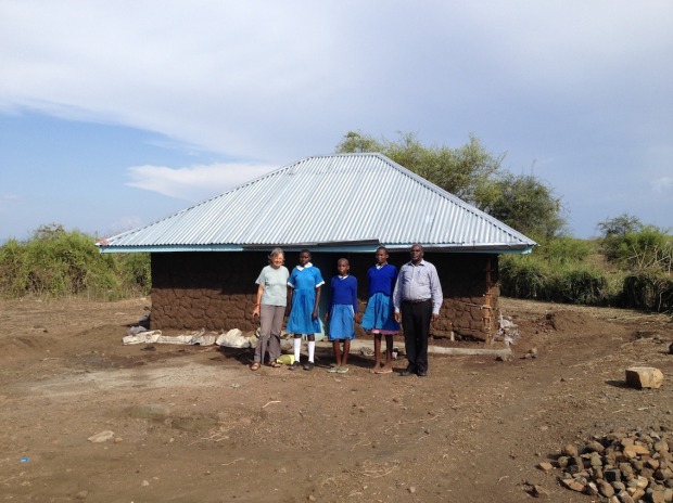 Three daughters with the  Head-teacher of †he local Primary School and Vice-Chair of Watu Kwa Watu in front of partially rebuild house