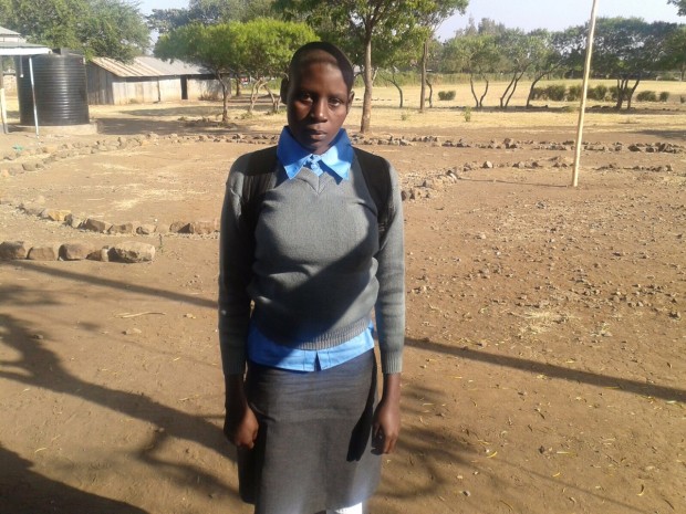 Isabel in her new High school uniform, with Kisuwi Primary in the background. 